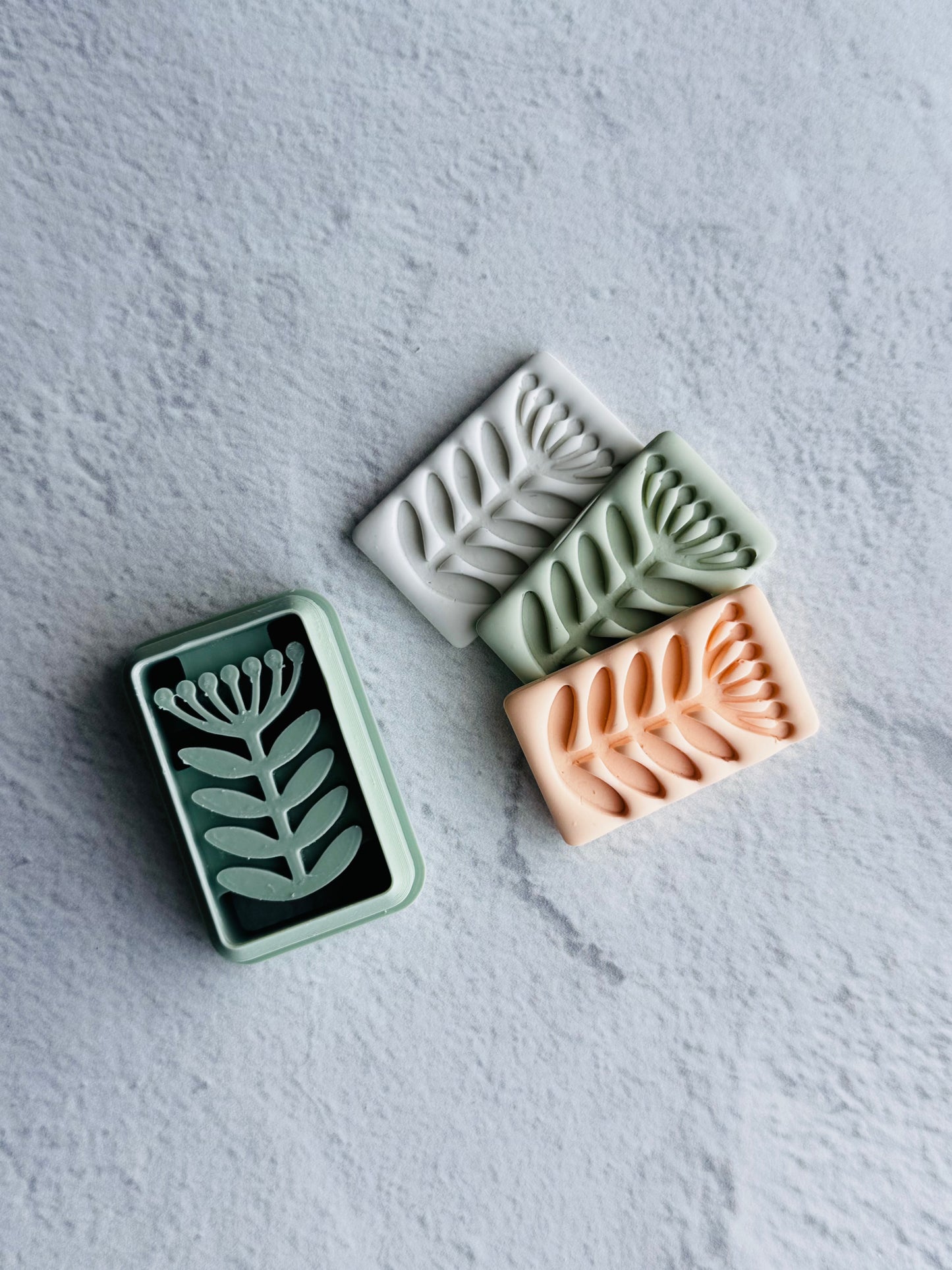 Three rectangular clay pieces with leaf patterns on a textured gray surface. Clay Cutters