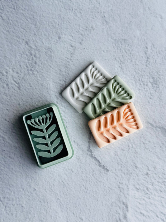 Three rectangular clay pieces with leaf patterns on a textured gray surface. Clay Cutters